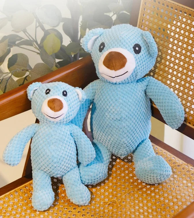 Two blue plush bear squeaky dog toys in large and small sizes sitting on a vintage woven rattan chair.