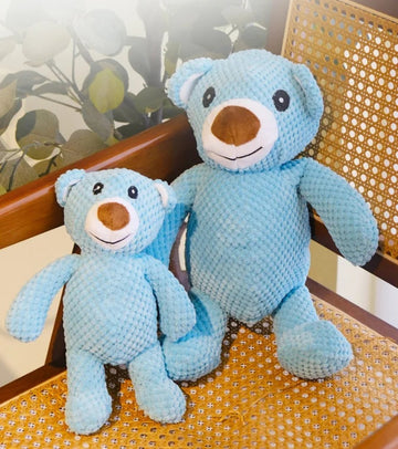 Two blue plush bear squeaky dog toys in large and small sizes sitting on a vintage woven rattan chair.