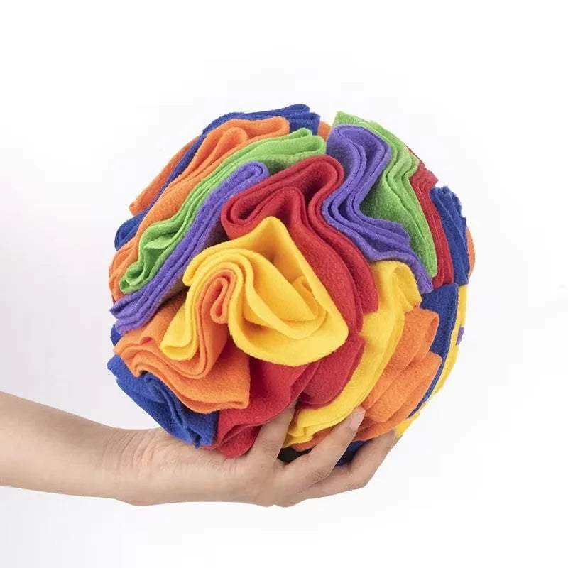 A hand holding a colorful multi-layered fleece snuffle ball toy for dogs