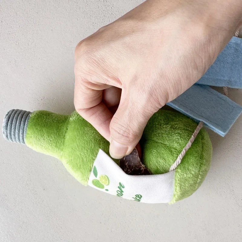 A hand hiding a dog treat inside the hidden nosework pocket of a green Lemon Sake plush snuffle toy.