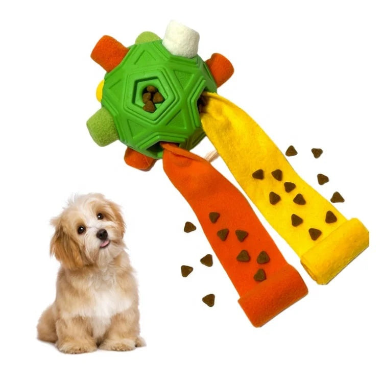 A small fluffy puppy sitting next to a green dog snuffle toy with treats falling out of unrolled fleece strips.